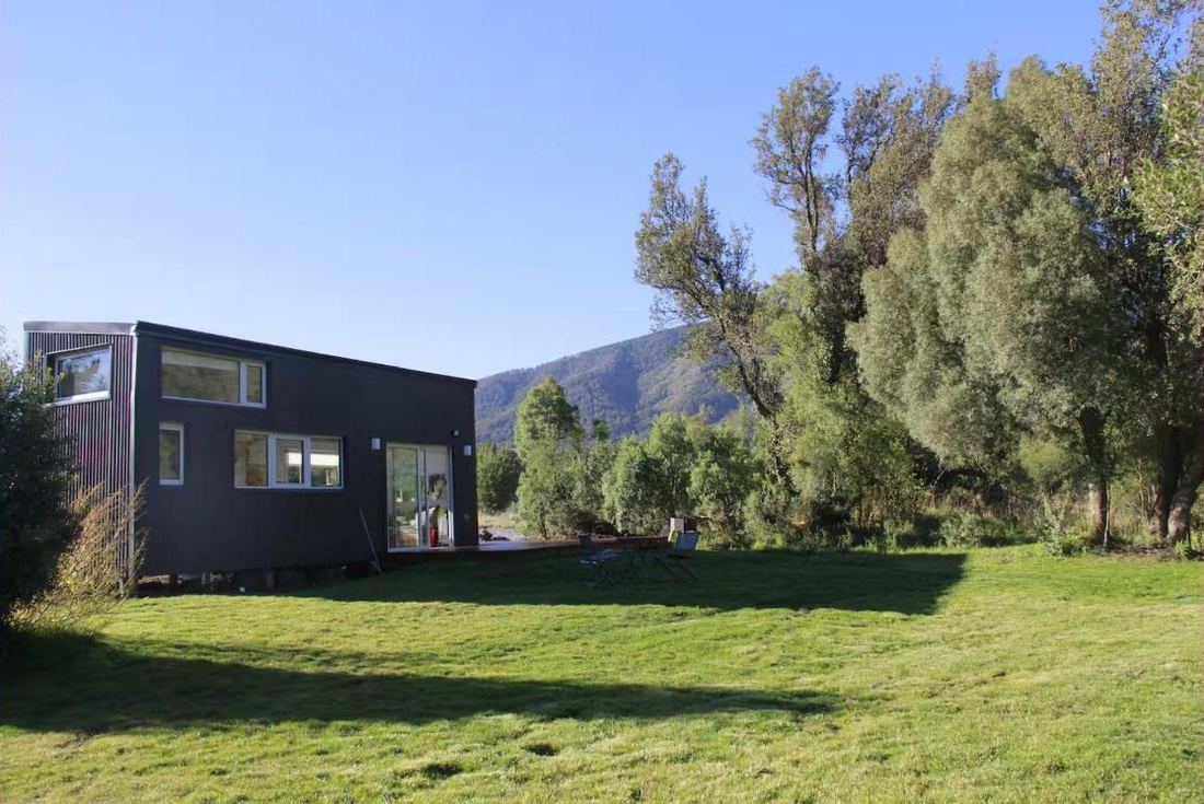 Tiny house negra sobre el césped, con árboles y el cerro detrás